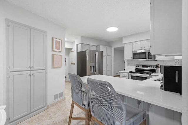 kitchen with stainless steel appliances, light countertops, visible vents, a peninsula, and a kitchen breakfast bar