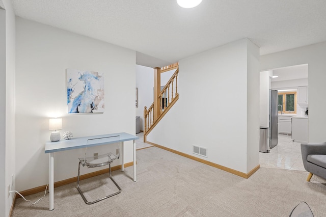 office featuring light carpet, baseboards, visible vents, and a textured ceiling