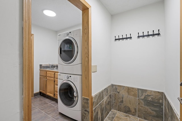 laundry room with stacked washer and dryer, dark tile patterned flooring, cabinet space, and a sink