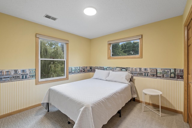 carpeted bedroom with a textured ceiling, wainscoting, and wallpapered walls