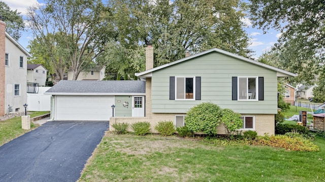 split level home featuring a chimney, aphalt driveway, an attached garage, a front yard, and brick siding