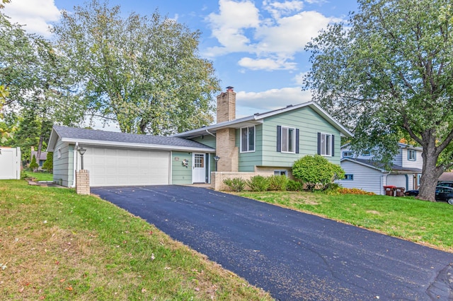 split level home featuring aphalt driveway, brick siding, a chimney, a front yard, and a garage