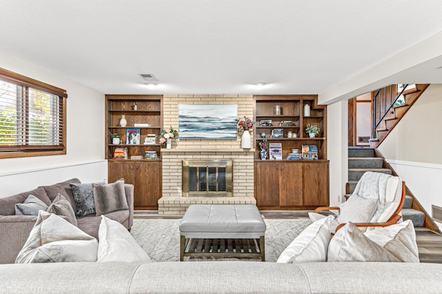 living area with built in features, visible vents, a brick fireplace, wood finished floors, and stairs