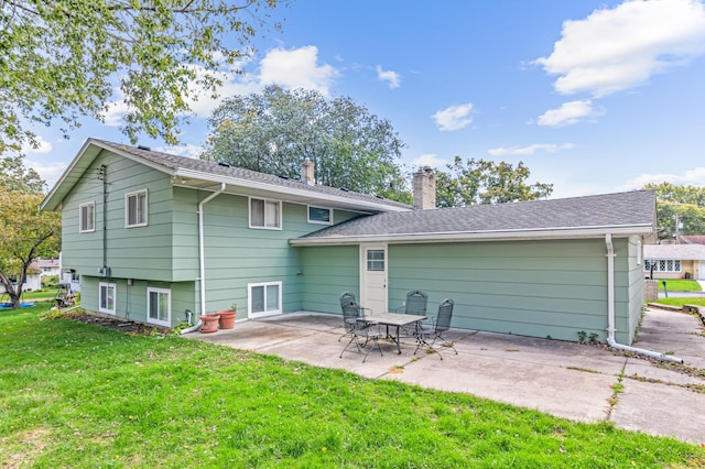 rear view of property featuring a shingled roof, a chimney, a lawn, and a patio