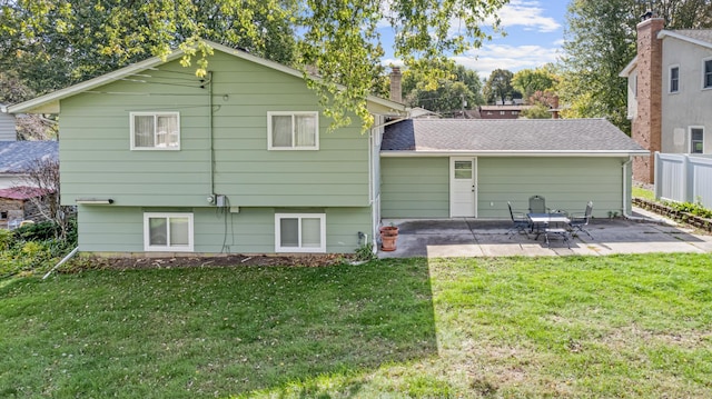 rear view of property featuring a shingled roof, a patio area, a lawn, and fence