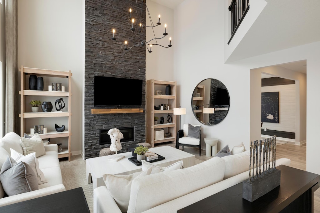 living room featuring a towering ceiling, light wood-style flooring, and a stone fireplace