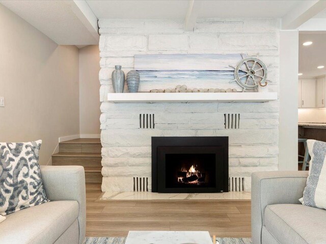 living area with baseboards, beamed ceiling, a stone fireplace, recessed lighting, and wood finished floors