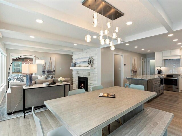 dining room with a stone fireplace, beam ceiling, light wood-style flooring, and recessed lighting