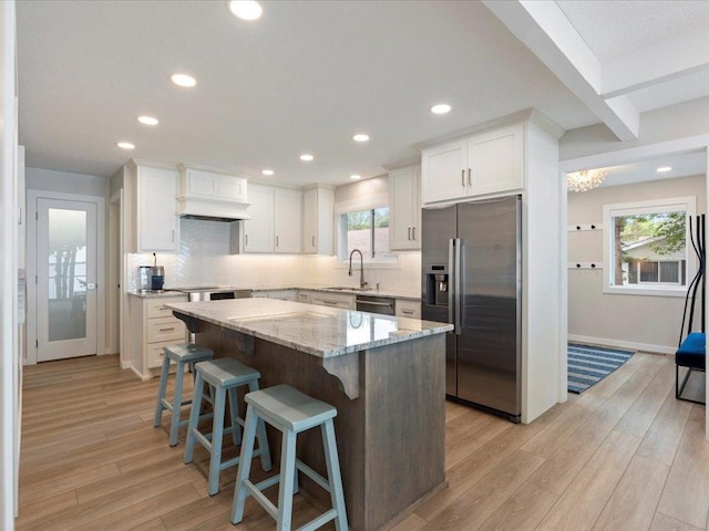 kitchen featuring a sink, stainless steel appliances, light wood-style floors, white cabinetry, and a center island