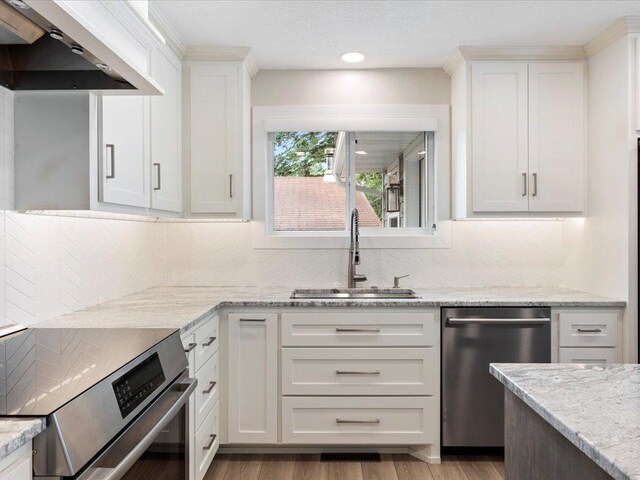 kitchen featuring a sink, stove, white cabinets, stainless steel dishwasher, and wall chimney exhaust hood