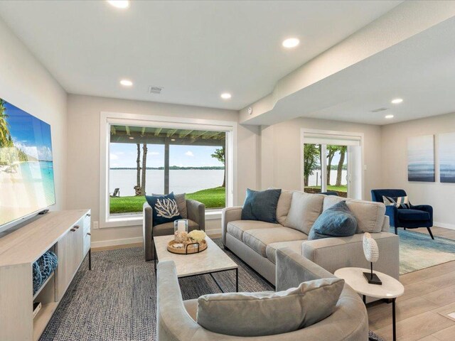 living room featuring recessed lighting, wood finished floors, a water view, and baseboards