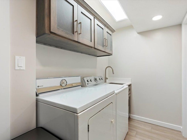 washroom with a sink, cabinet space, light wood-style floors, separate washer and dryer, and baseboards