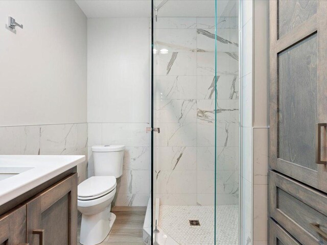 bathroom featuring a marble finish shower, toilet, tile walls, and vanity