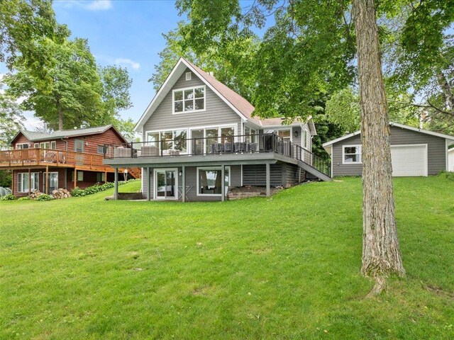 rear view of property with a detached garage, a wooden deck, stairs, a yard, and an outdoor structure