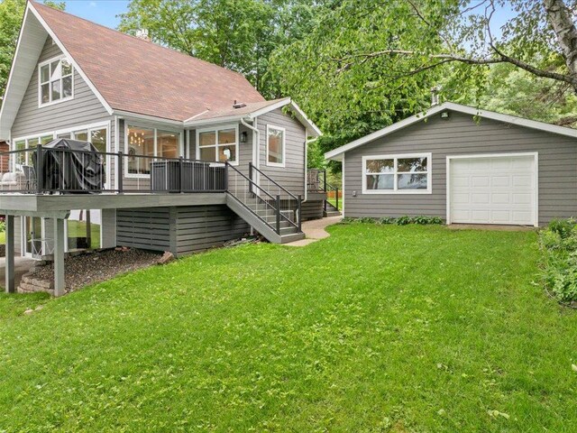 back of property featuring a lawn, a detached garage, stairway, roof with shingles, and a wooden deck