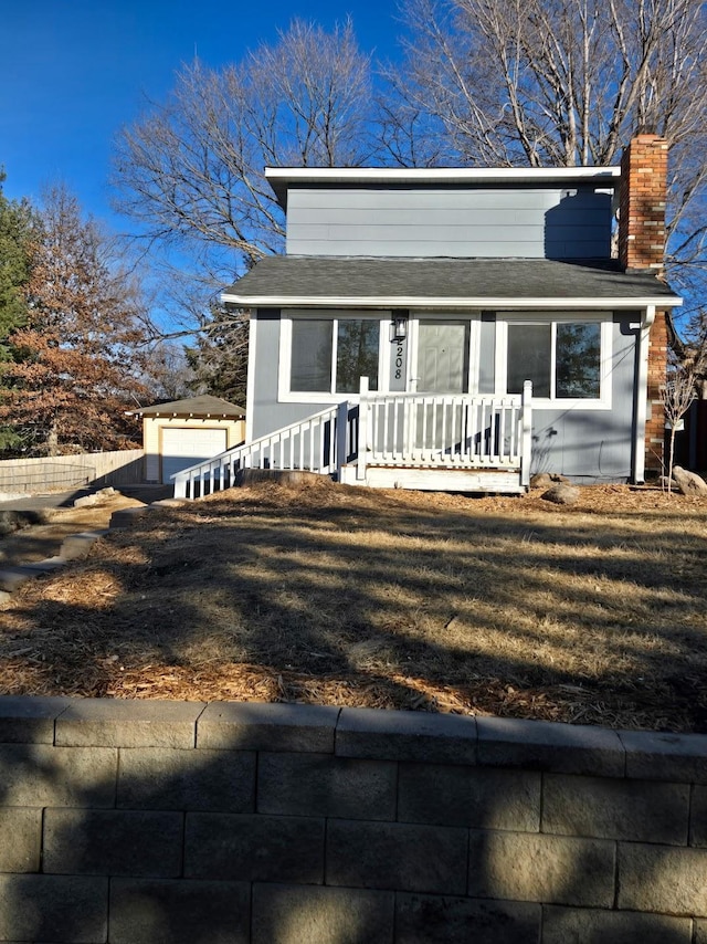 view of front of home with an outbuilding, a porch, a shingled roof, a front lawn, and a chimney