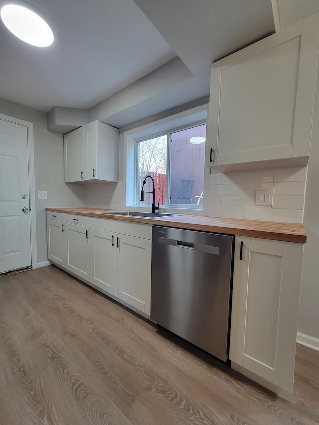 kitchen featuring a sink, wood counters, light wood-style floors, stainless steel dishwasher, and tasteful backsplash