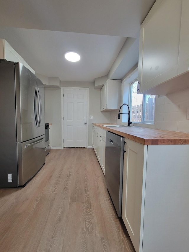 kitchen with light wood-style flooring, stainless steel appliances, a sink, white cabinets, and wooden counters