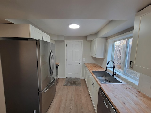 kitchen with appliances with stainless steel finishes, a sink, butcher block counters, and white cabinets