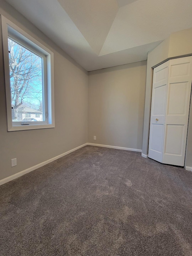 unfurnished bedroom featuring carpet, baseboards, vaulted ceiling, and a closet