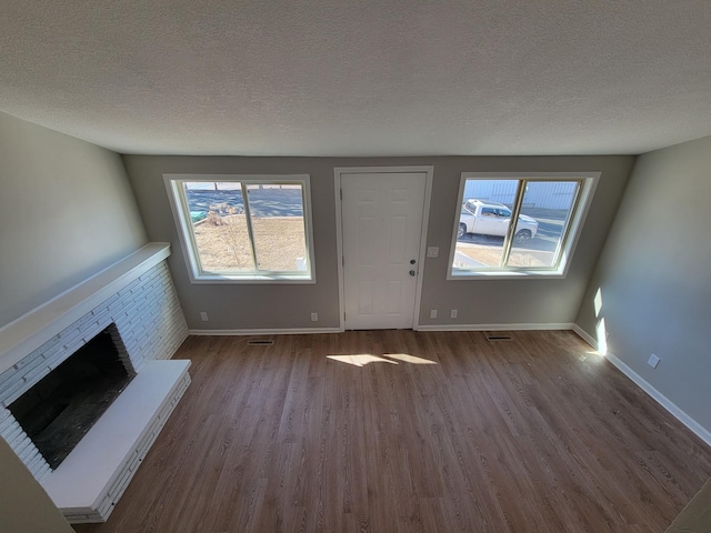 unfurnished living room featuring a textured ceiling, dark wood-style flooring, a brick fireplace, and baseboards