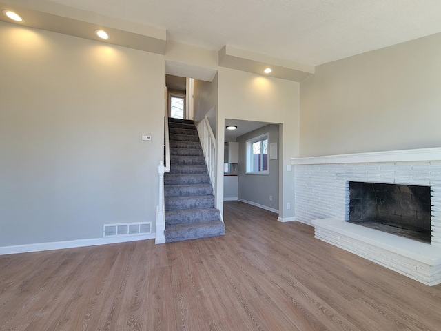 unfurnished living room with baseboards, visible vents, wood finished floors, stairs, and a brick fireplace