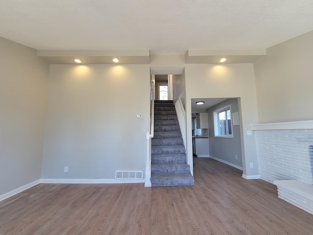 stairway featuring a textured ceiling, wood finished floors, visible vents, baseboards, and a brick fireplace