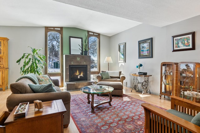 living room with a tiled fireplace, lofted ceiling, wood finished floors, and a textured ceiling