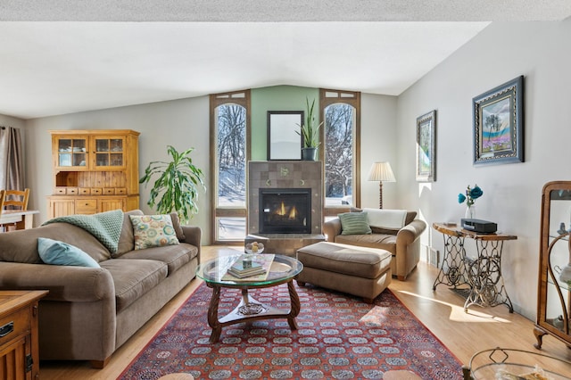 living room with a tiled fireplace, vaulted ceiling, and light wood finished floors