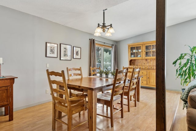 dining room with a chandelier, baseboards, light wood-style floors, and vaulted ceiling