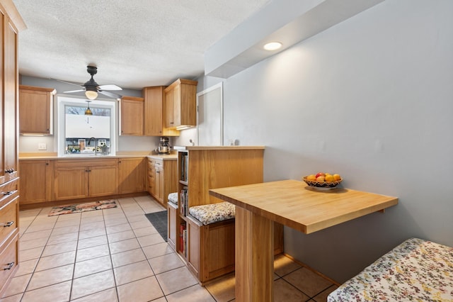 kitchen featuring light tile patterned floors, a ceiling fan, a peninsula, a textured ceiling, and a kitchen breakfast bar