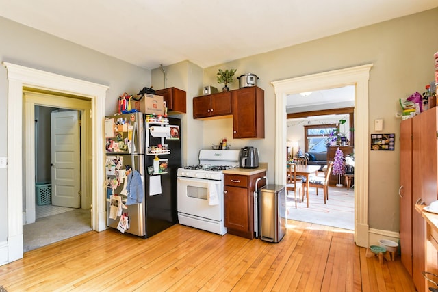 kitchen with white gas stove, light countertops, freestanding refrigerator, light wood finished floors, and brown cabinetry