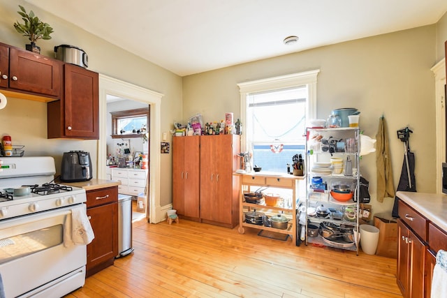 kitchen with light countertops, light wood-type flooring, white range with gas stovetop, and a healthy amount of sunlight