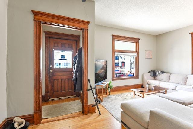 living area featuring a textured ceiling, light wood finished floors, and baseboards