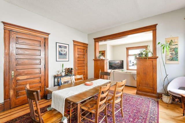 dining room featuring light wood-type flooring and a textured ceiling