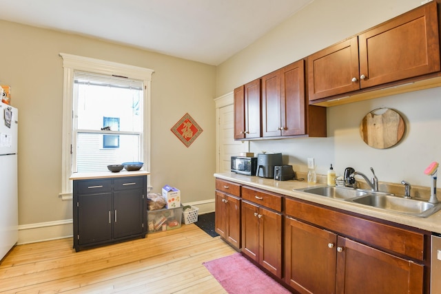 kitchen with stainless steel appliances, light wood finished floors, a sink, and light countertops