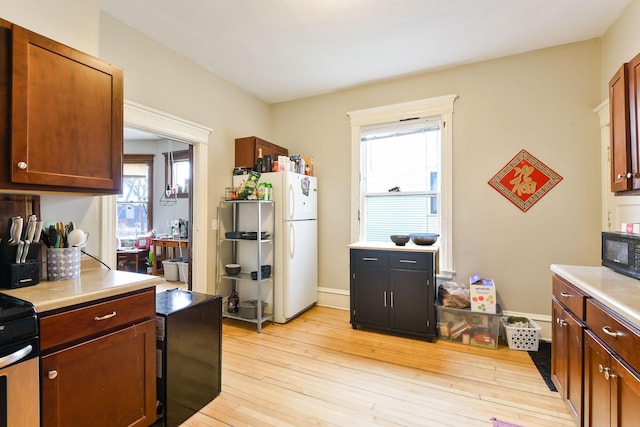 kitchen with freestanding refrigerator, black microwave, light countertops, and light wood-style flooring