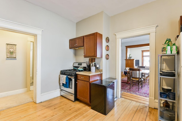 kitchen with brown cabinets, gas range, baseboards, and light wood finished floors