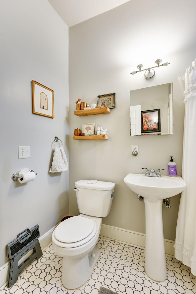 half bathroom with toilet, baseboards, and tile patterned floors