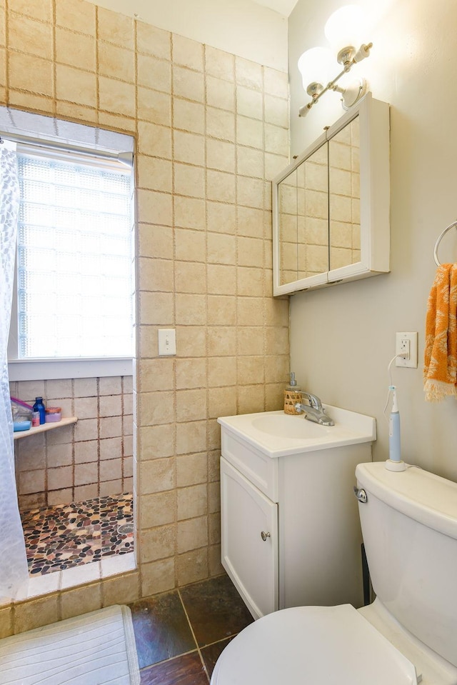 bathroom with toilet, tile walls, tiled shower, and vanity