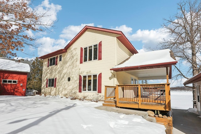 snow covered back of property featuring a garage and a wooden deck