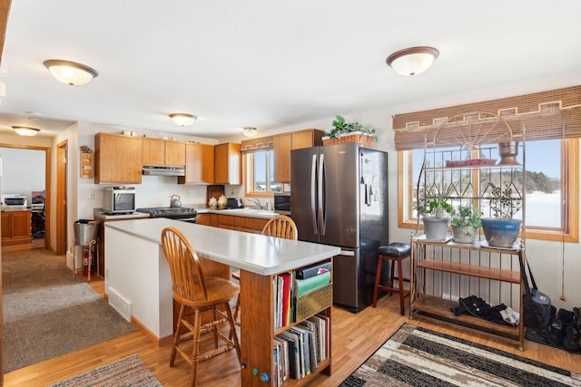 kitchen featuring under cabinet range hood, a sink, light wood-style floors, light countertops, and freestanding refrigerator