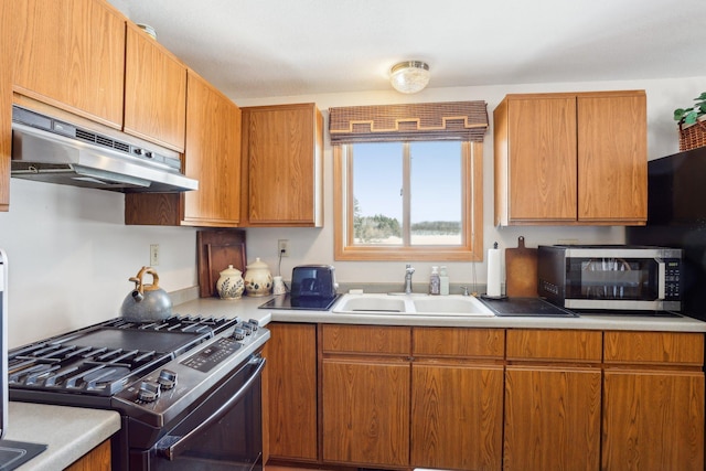 kitchen with appliances with stainless steel finishes, light countertops, a sink, and under cabinet range hood