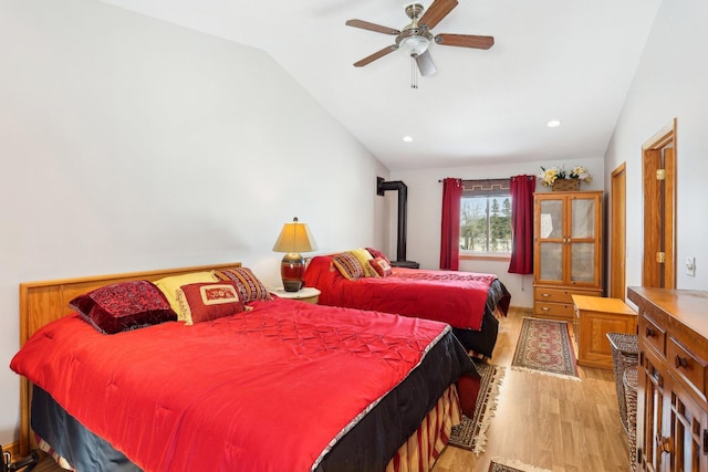 bedroom featuring ceiling fan, light wood-style flooring, recessed lighting, vaulted ceiling, and a wood stove