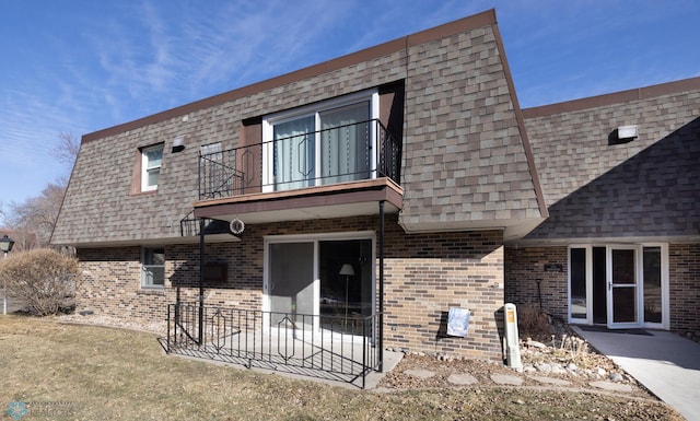 back of property with brick siding, a balcony, mansard roof, and roof with shingles