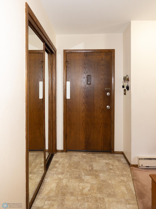 hallway featuring stone finish floor, baseboards, and a baseboard radiator