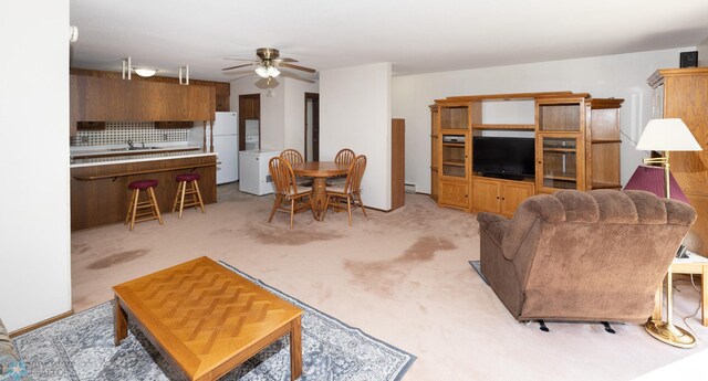 living area with a baseboard heating unit, a ceiling fan, and light carpet