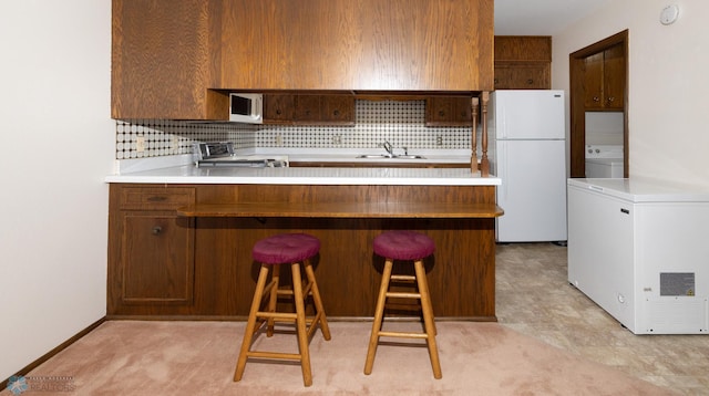 kitchen featuring white appliances, a peninsula, washer / dryer, a sink, and tasteful backsplash