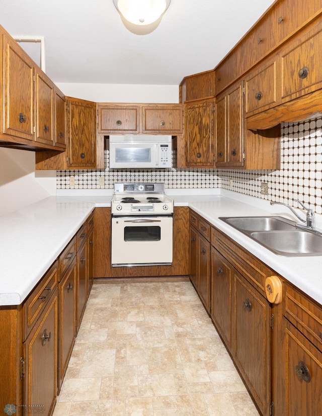 kitchen featuring light countertops, decorative backsplash, brown cabinetry, white appliances, and a sink