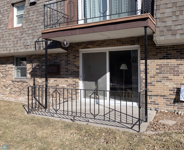 doorway to property featuring a balcony, mansard roof, brick siding, and a shingled roof